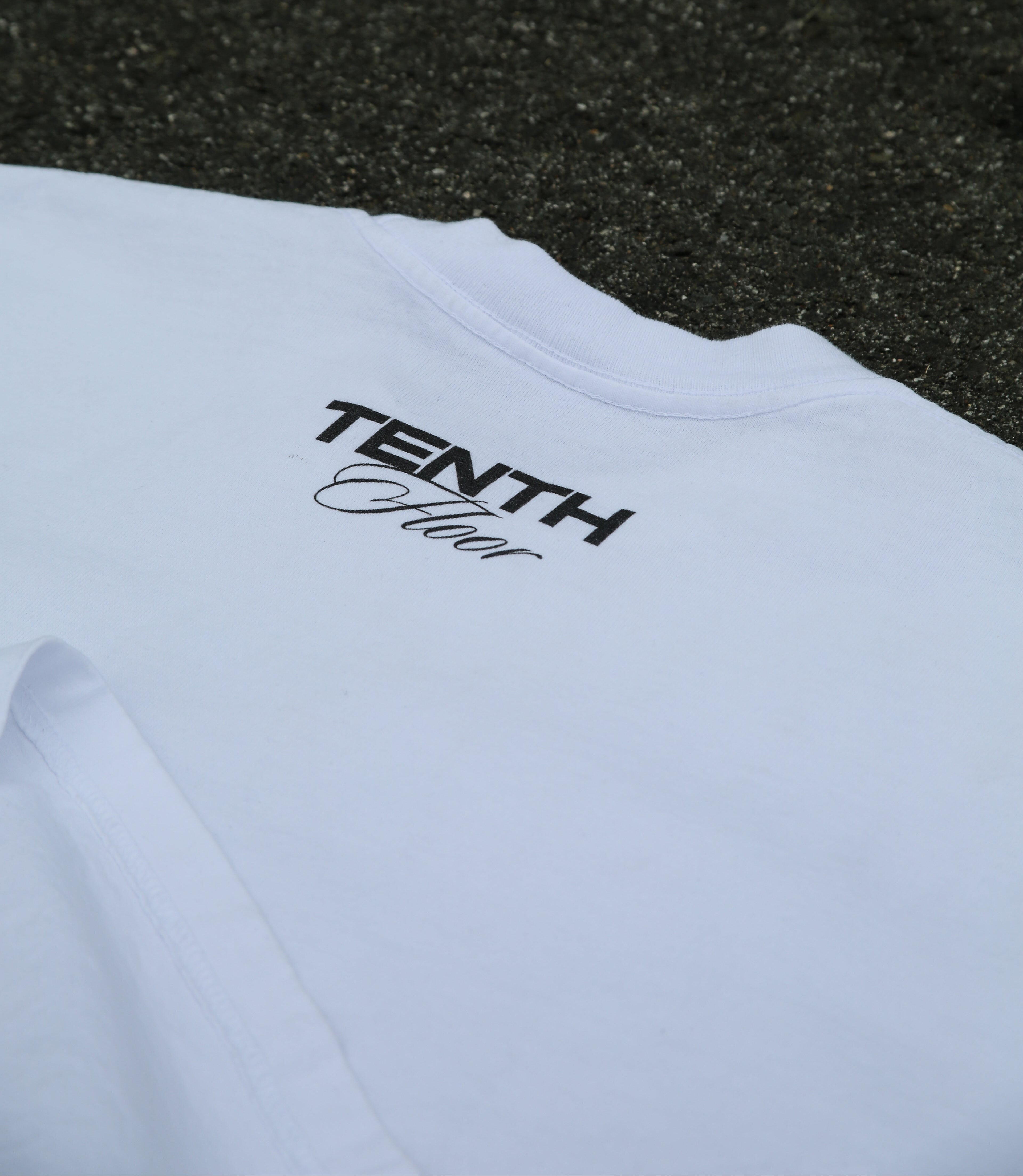 White t-shirt with 'Tenth Floor' logo on a textured black surface